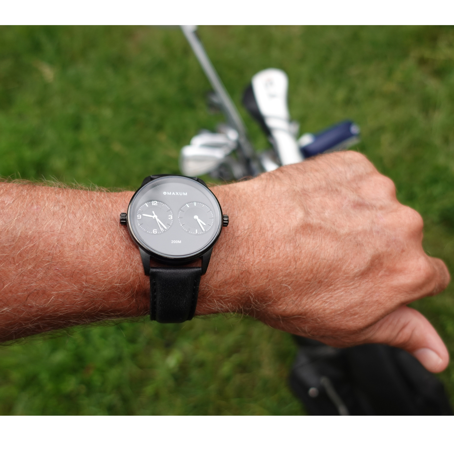 Maxum x Taylor Steele collab- black analog watch with a black dial, black case, and black leather band, branded with 'MAXUM' on the top and indicating '200M' water resistance. Person wearing on a golf course