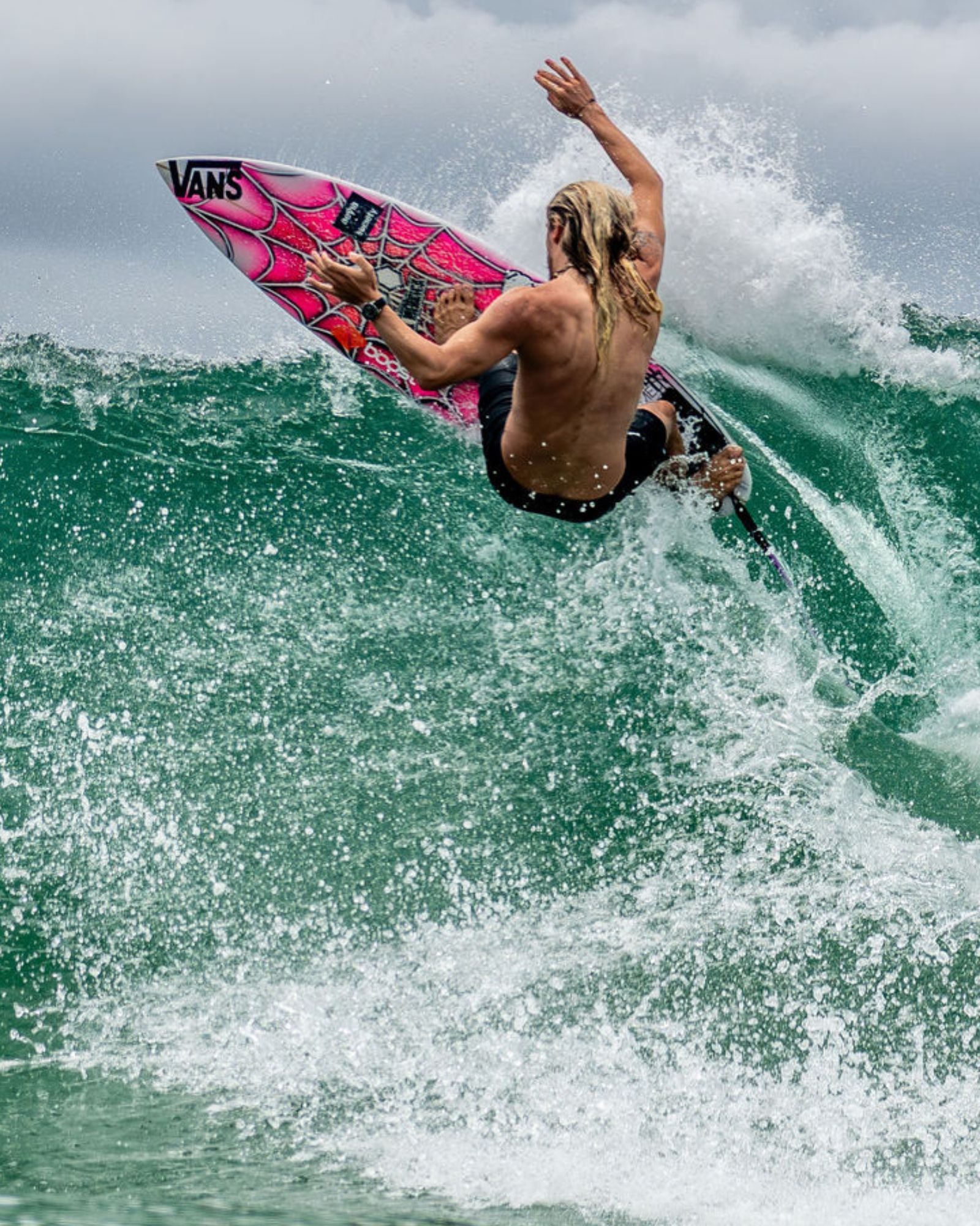 Kyuss King riding a wave with a pink and black Vans surfboard wearing Maxum Prince silver-tone casing watch with a black dial and black silicone strap, indicating 200m water resistance and featuring a date display.