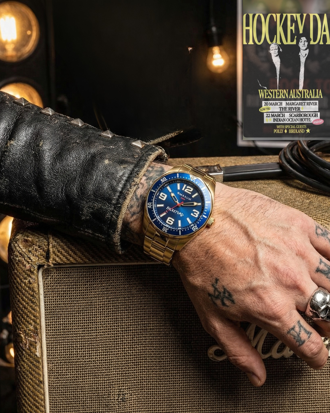Hand wearing Hockey Dad x Maxum collab gold watch with blue face on a textured surface, with a background featuring a gig poster 'Hockey Dad'.