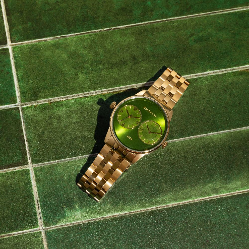 Maxum x Taylor Steele Collab gold-tone watch with a green dial and a stainless steel bracelet on green suede background