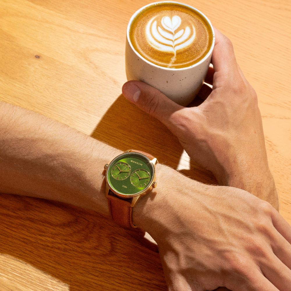 Maxum Taylor Steele Collaboration Watch with a green dial, gold-tone case, and brown leather band, wrist shot with coffee