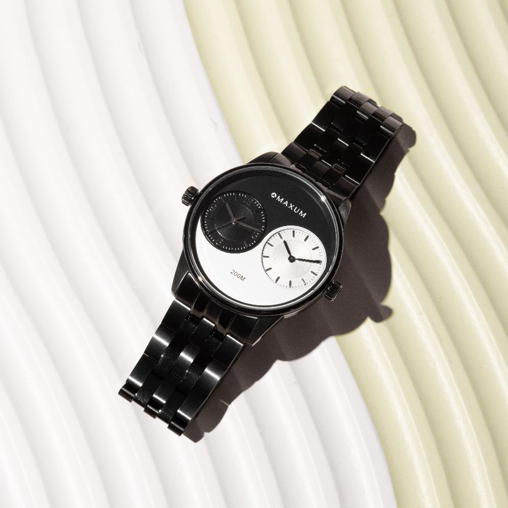 Maxum x Taylor Steele Collab analogue watch with a black stainless steel bracelet, black case, and a matte black dial featuring ying yang design and a dual timekeeping system. On textured wave back ground