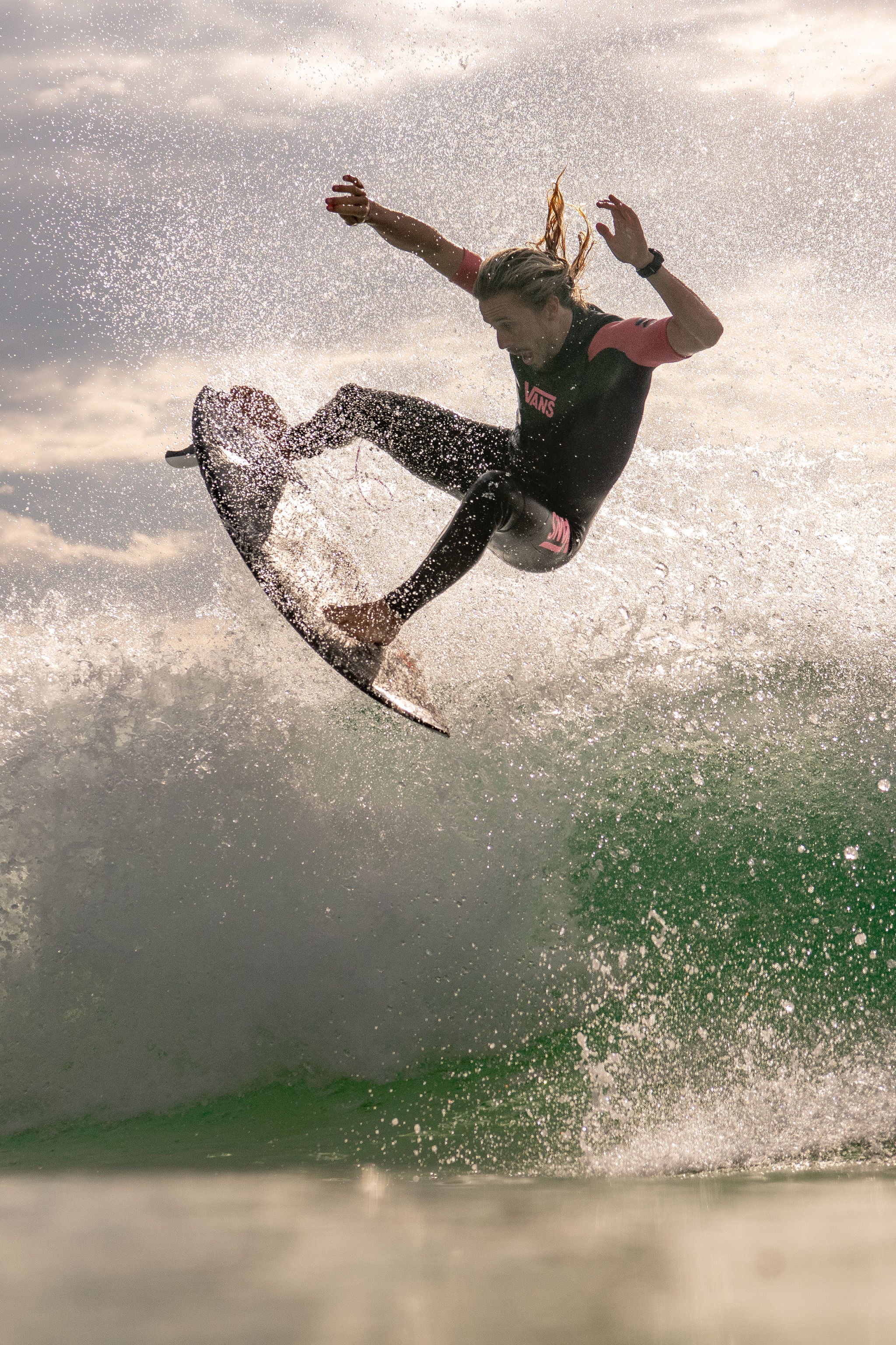 Maxum Basalt Black Digital Watch worn by surfer Kyuss King in the ocean in mid-air with a splash of water and