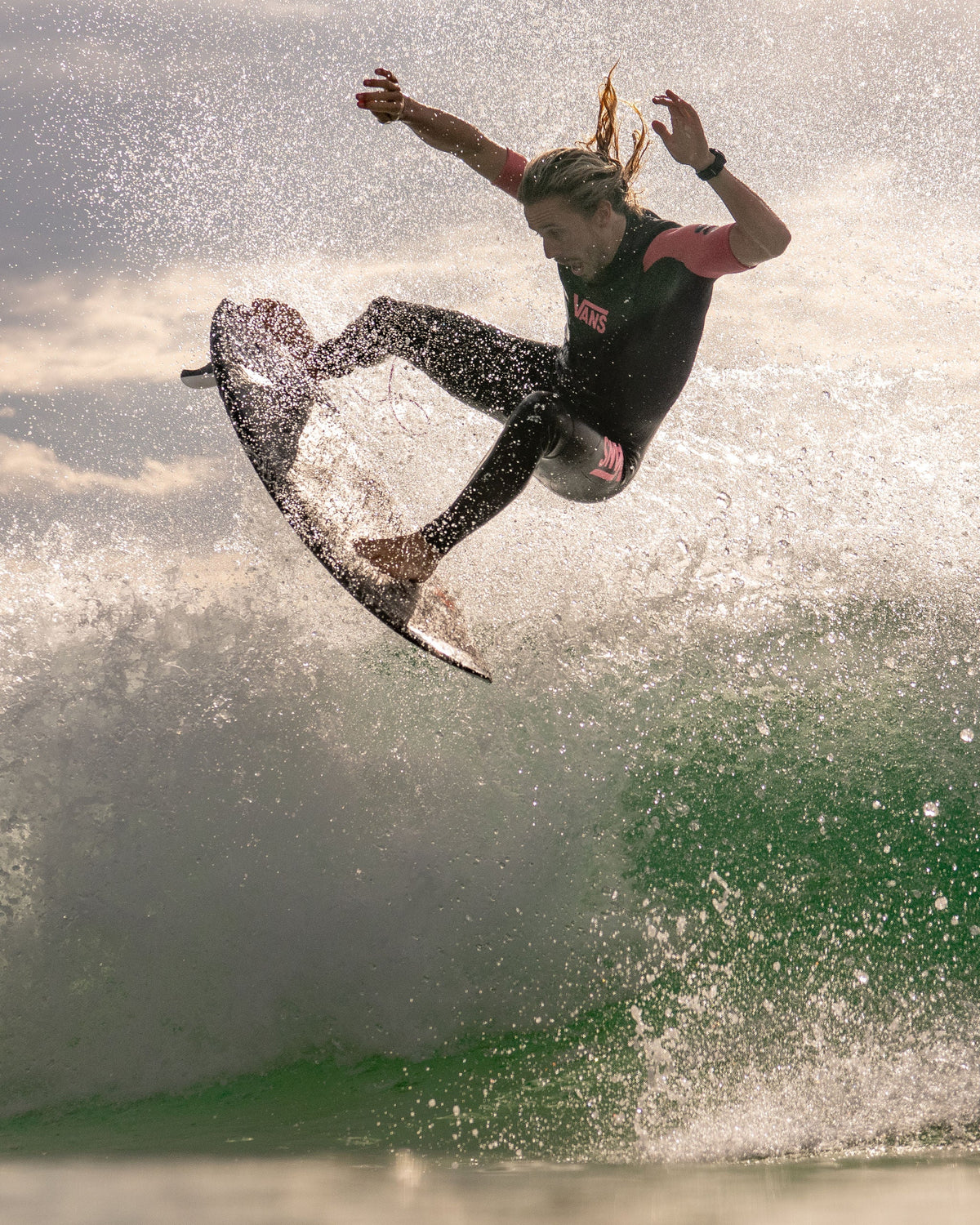 Maxum Basalt Black Digital Watch worn by surfer Kyuss King in the ocean in mid-air with a splash of water and