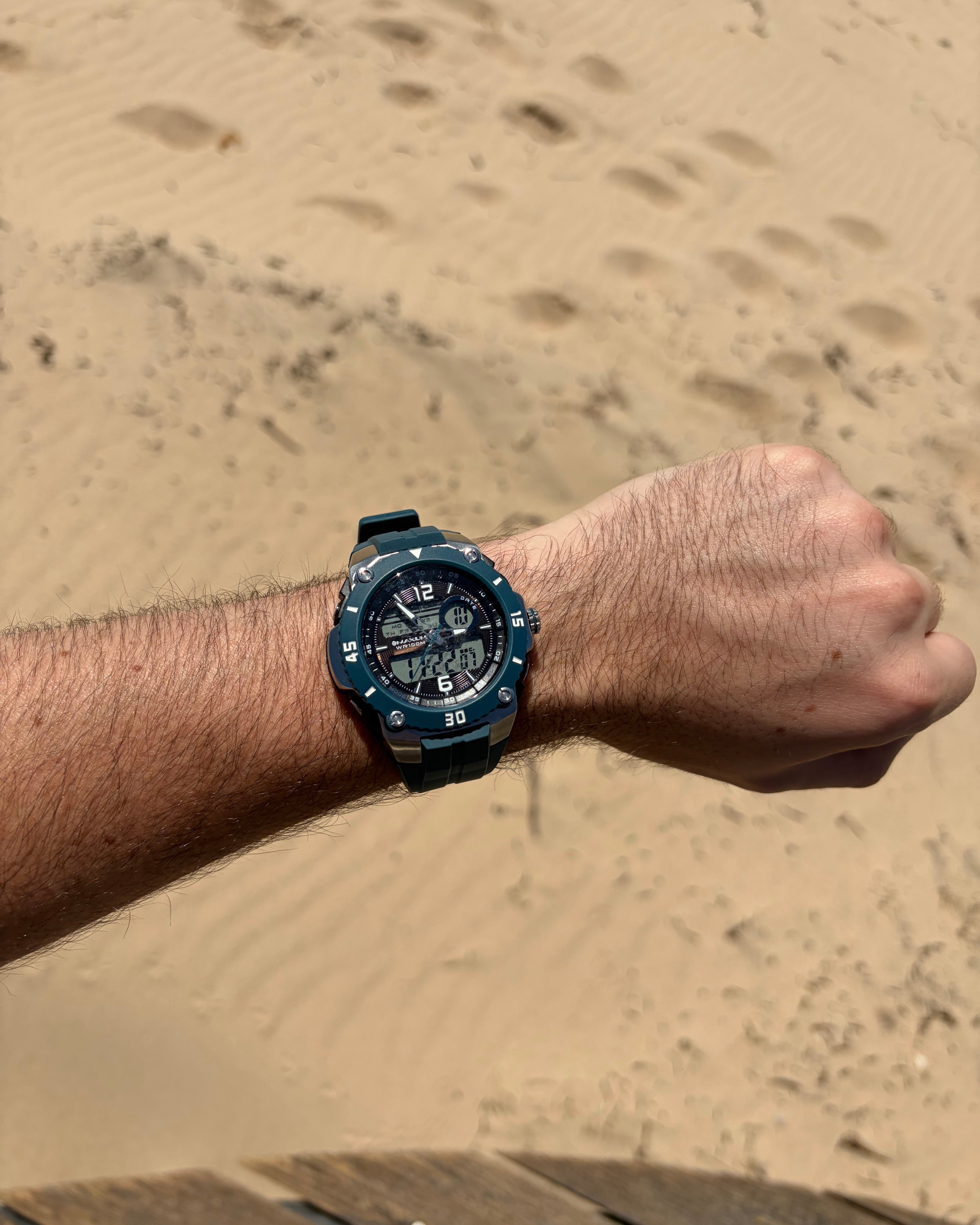 Maxum Maverick Blue Analogue Digital Watch with a silver and blue-tone case, a digital display, and a blue resin strap on Hand wearing with a sandy background