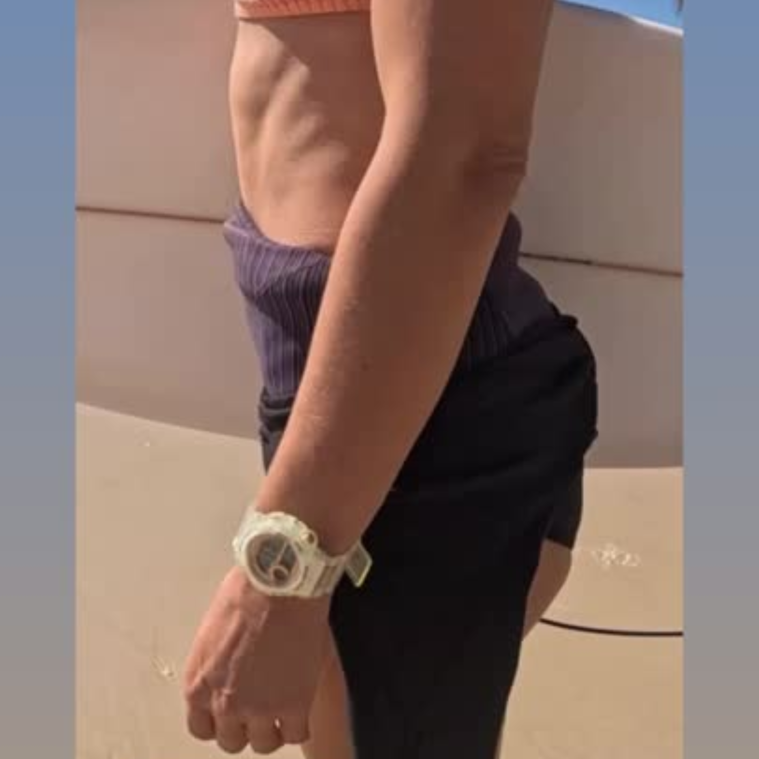 Maxum Endurance digital watch with a clear band and case, featuring a rose gold and white digital display, and buttons for various functions. Worn by female holding surfboard at beach 